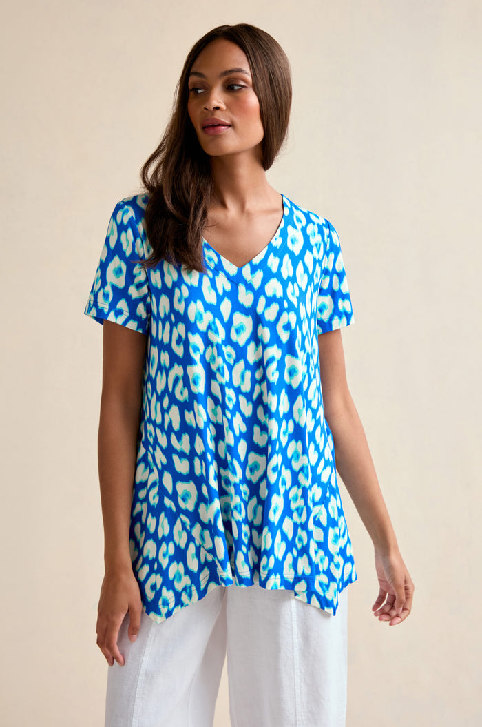 A woman showcases the Abstract Leopard Print Jersey Top in blue and white with white pants against a plain background, highlighting this stylish women’s summer top.