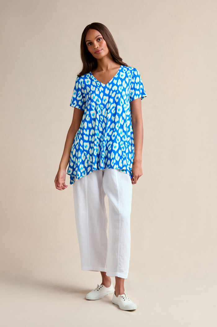 Woman stands against a plain background, wearing the Abstract Leopard Print Jersey Top in blue and white, paired with white wide-leg pants and white sneakers.