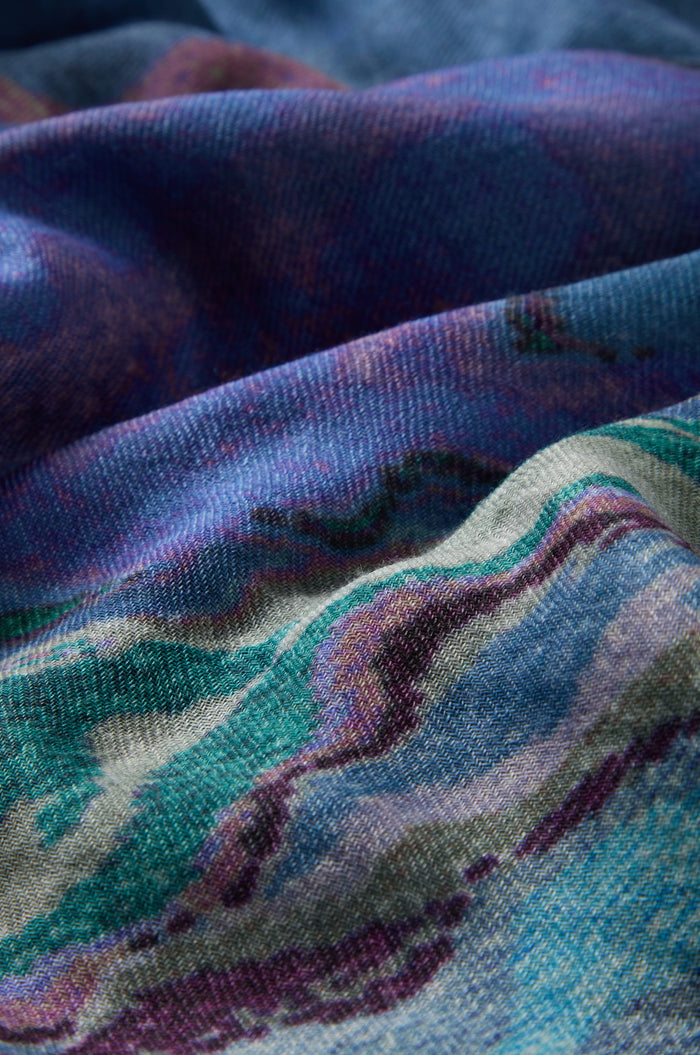 Close-up of the Agate Wool Scarf, showcasing its textured fabric with a multicolored abstract pattern in shades of blue, purple, teal, and cream. The woven details and folds highlight the Indian textile's agate-inspired print, giving it a unique artistic touch reminiscent of luxurious wool-silk accessories.
