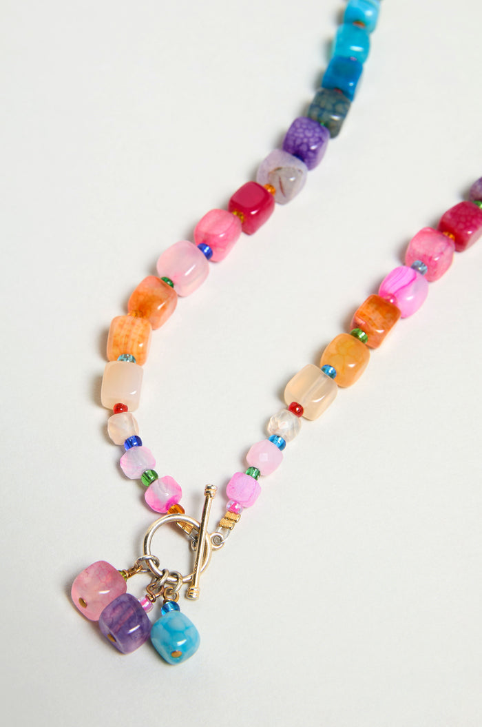 The Artisanal Rainbow Agate Toggle Necklace, handmade in Scotland with irregularly shaped rainbow agate beads and a gold toggle clasp, is displayed on a light background.