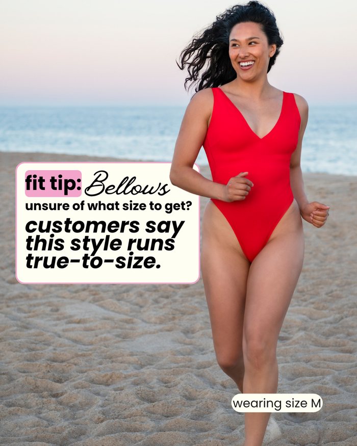 Front view of red Bellows Plunge High-Cut One Piece showcasing deep V and high-cut leg on beach wearing size M runs true to size