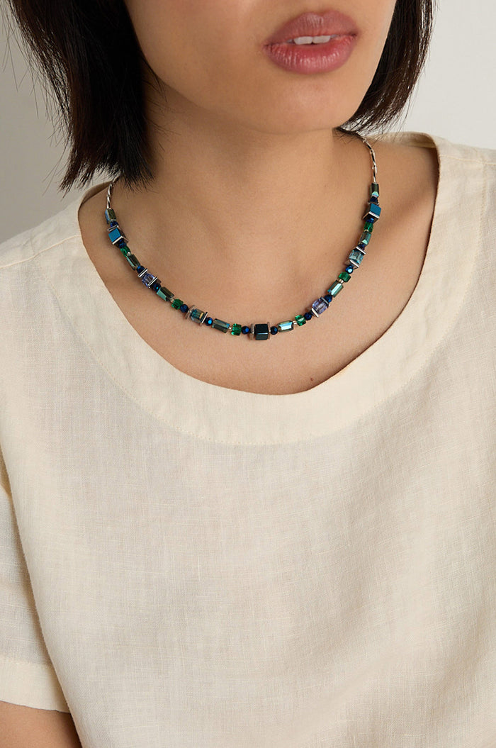 A woman wears a cream top and the Blue Hematite Necklace, handmade in Scotland, featuring blue and green square beaded accents.