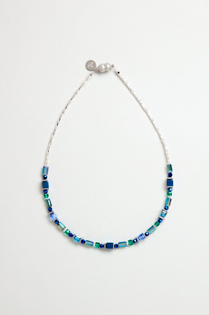 The Blue Hematite Necklace features blue and green square and rectangular beads, faceted glass crystals on a thin white string, handmade in Scotland with a small silver charm and clasp.