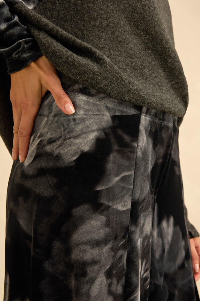 Wearing a dark grey sweater and the Blurred Floral Velvet Bubble Trousers, which feature sculptural volume, a person rests their hand on their hip.