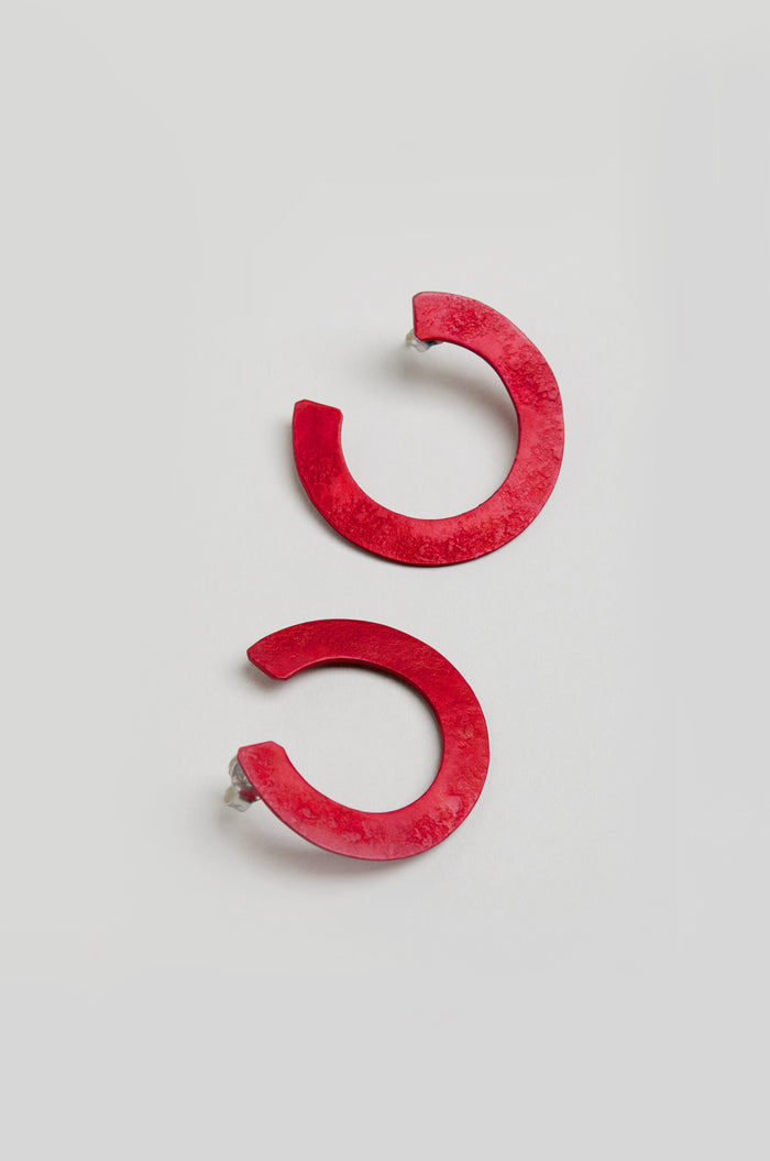 The C Curve Earrings are bold, red, semi-circular hoops with post backs, shown on a light background—modern accessories designed for a standout look.