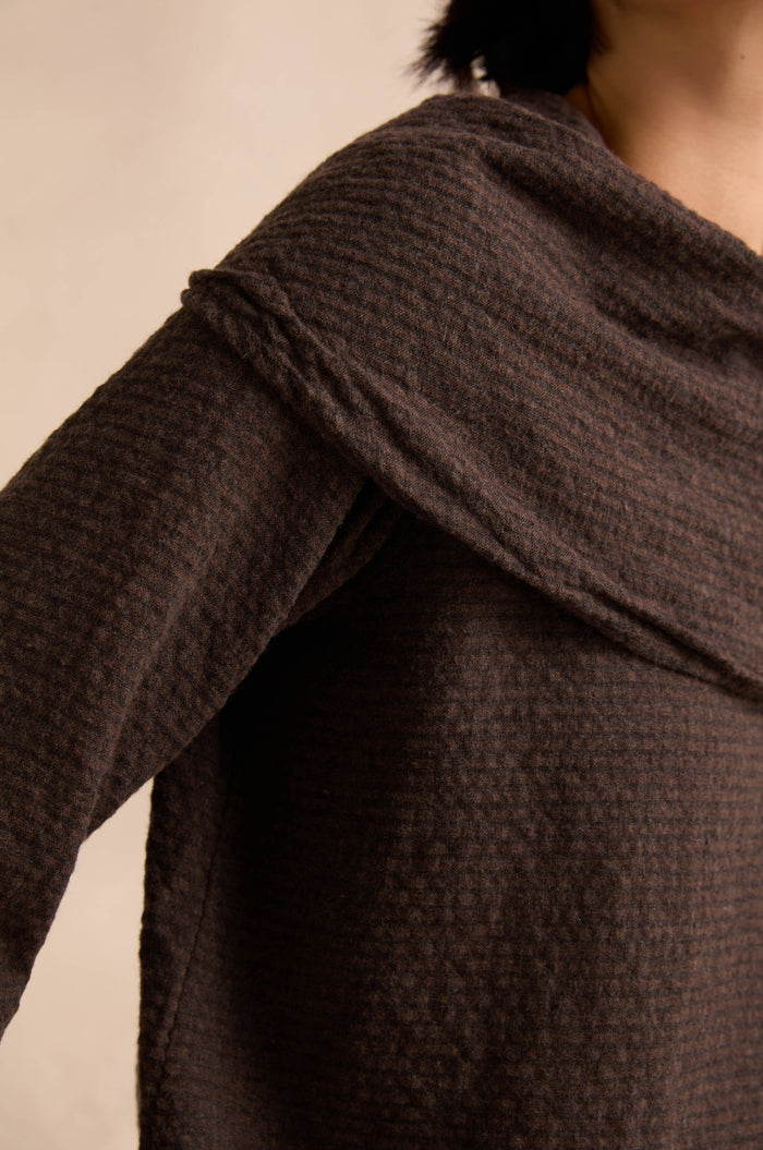 Close-up of a person wearing the Chocolate Draped Neck Top, featuring a textured dark brown knit with a wide, asymmetric draped neckline, shown from shoulder to upper chest against a neutral background.