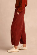 A person wearing the Conker Pinwale Cord Bubble Trouser, styled with a red sweater and white sneakers, stands sideways with hands in pockets against a neutral background.