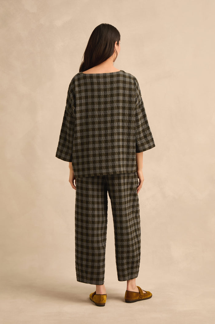 A person stands with their back to the camera, wearing the Crinkle Check Boxy Top in an oversized fit, paired with matching pants and yellow slip-on shoes against a neutral background.