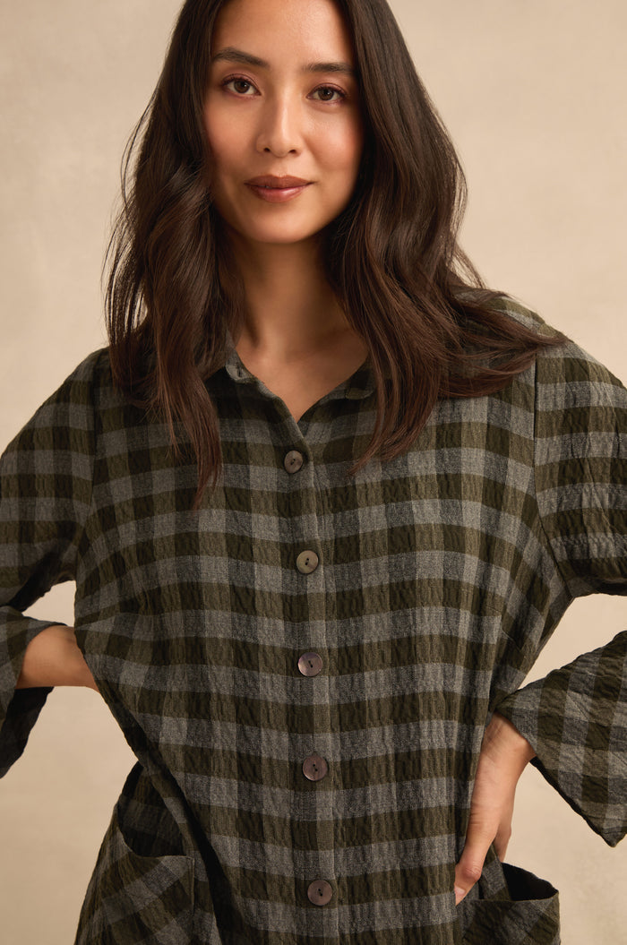 A woman with long dark hair stands against a neutral background, wearing the Crinkle Check Flared Jumpsuit and posing with her hands on her hips.