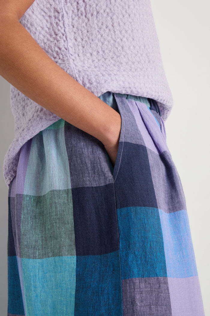 A person wearing a textured light purple top and Cross Dye Check Linen Wide Trousers stands with one hand in their pocket.