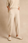 Wearing the Ecru Ponte Bubble Trousers, a matching sweater, and white sneakers, a person stands with hands in pockets against a neutral background.