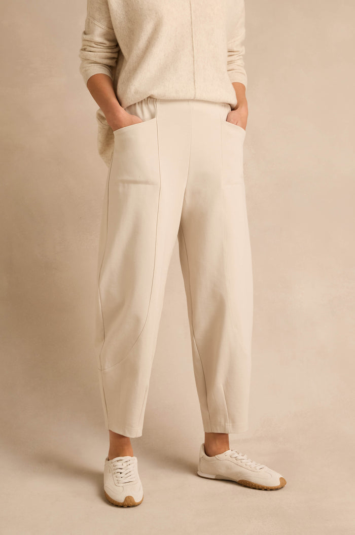 Wearing the Ecru Ponte Bubble Trousers, a matching sweater, and white sneakers, a person stands with hands in pockets against a neutral background.