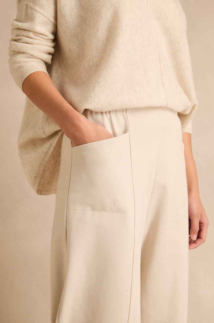 Person wearing a loose, cream-colored top and wide-leg, high-waisted Ecru Ponte Bubble Trousers with one hand in the pocket, shown from mid-torso to knee.