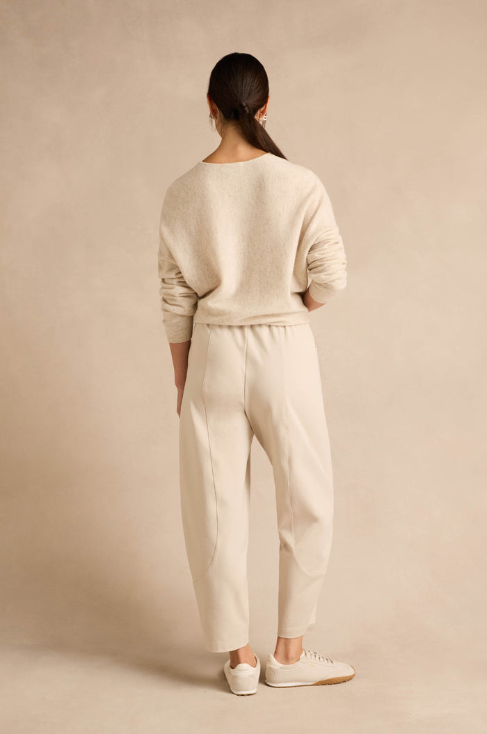 Person standing with back to camera, wearing a light beige sweater paired with Ecru Ponte Bubble Trousers and white sneakers against a neutral background.