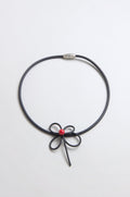 The Flower Necklace features a bow-shaped center with a single red bead, reminiscent of handmade ceramic jewelry, displayed against a plain light background.