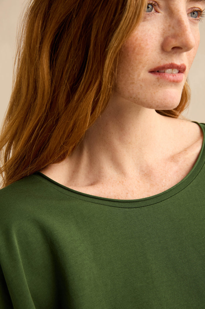A woman with long red hair, shown from the shoulders up and looking slightly to the side, is wearing the Forest Cotton Jersey Pocket Top.