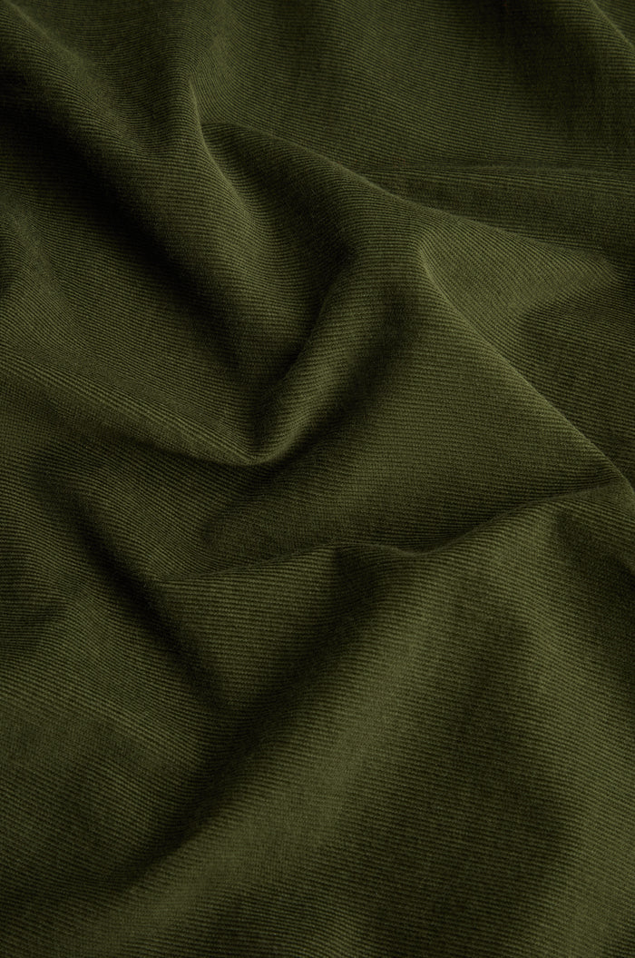 Close-up of dark green pinwale corduroy fabric with visible ridges and gentle folds, showcasing the signature texture of the Forest Pinwale Cord Bubble Trousers.