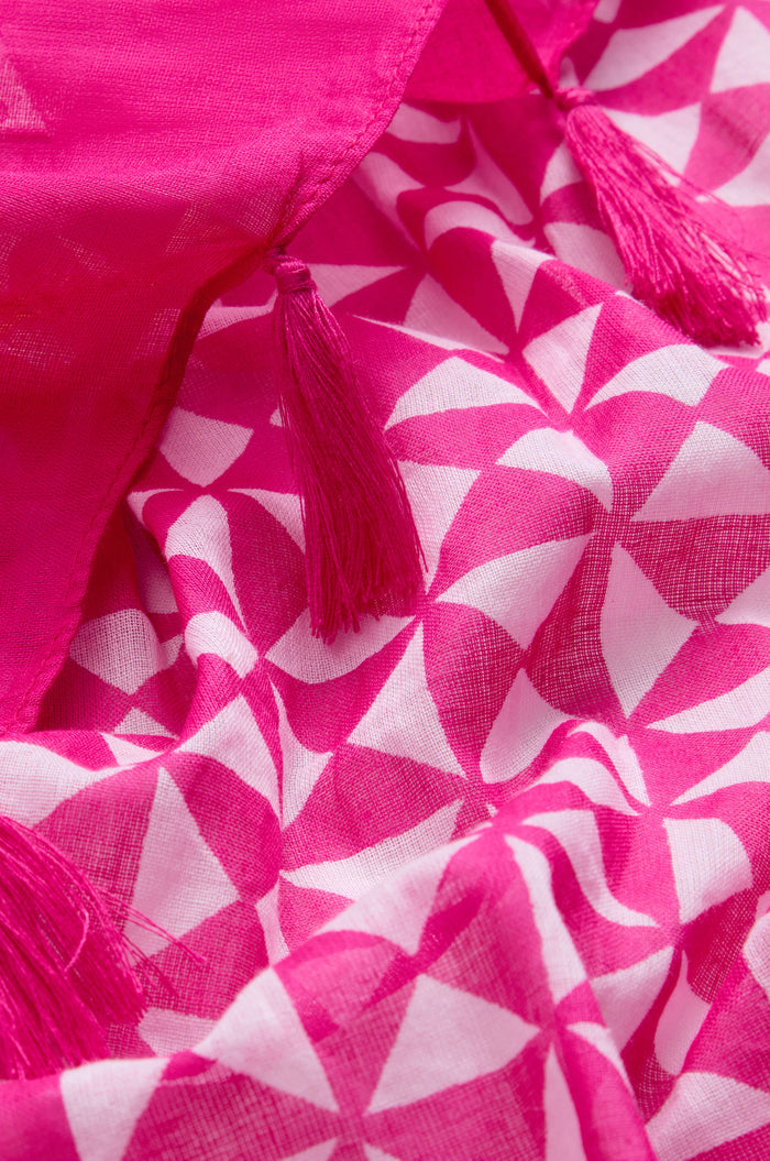 A close-up of the Fuchsia Tassel Cotton Scarf, crafted in cotton with a pink and white geometric print and finished with delicate fuchsia tassel edging.
