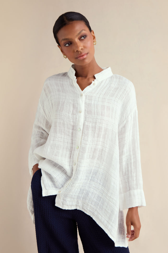 A woman models the Gauzy Linen Relaxed Shirt—an oversized white top—paired with dark pants, standing against a plain light background and looking slightly to the side.