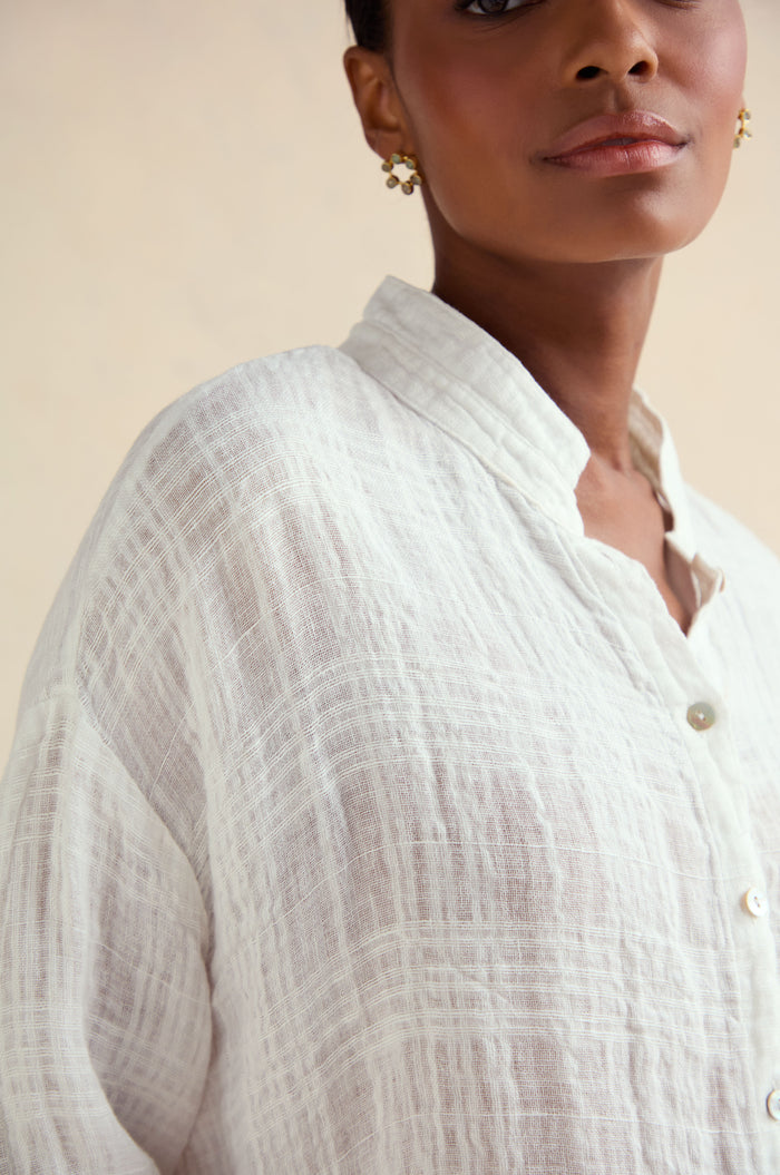Close-up of a person wearing the Gauzy Linen Relaxed Shirt—an oversized white collared top—paired with gold earrings against a neutral background.