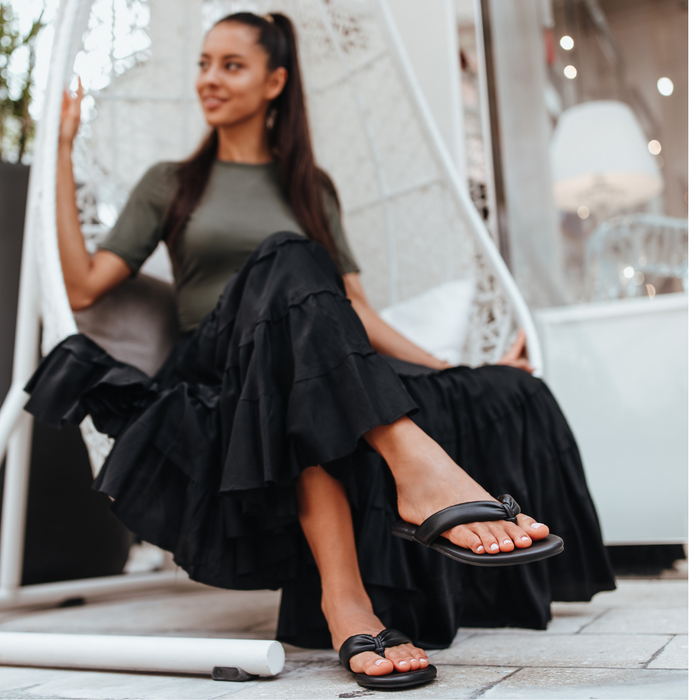 Woman in a black dress sitting in a chair smiling in black flip-flop sandals