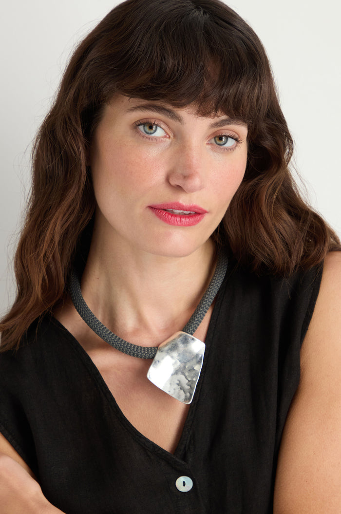 A woman with long brown hair in a black sleeveless top models the Hammered Silver Pendant Cord Necklace, looking at the camera against a plain background.