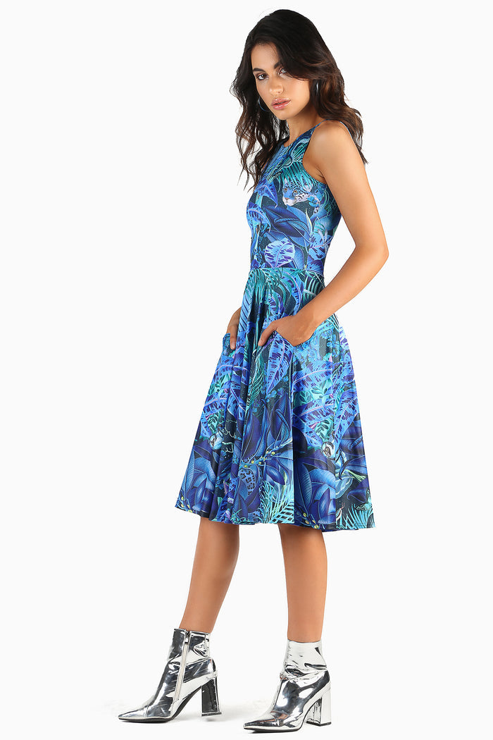 Woman wearing a dress with a blue and green jungle print featuring birds and foliage on a white background