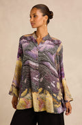 A woman stands against a neutral background wearing the Impressionist Print Flared Shirt—a loose, long-sleeve top crafted from a luxurious cupro and viscose blend with a collar and button front—paired with black pants.