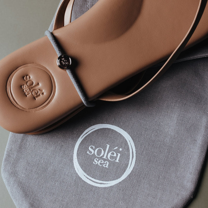 Close-up of the tan INDIE thong sandal showcasing its embossed Solei Sea logo with a reusable cotton drawstring bag