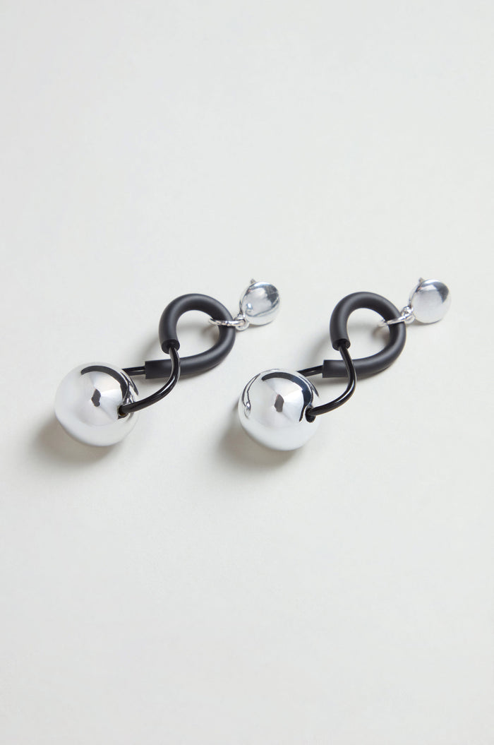 The Infinity Earrings display a sculptural design with black curved links connected to polished silver spheres and smaller silver bead studs, all set against a light background.