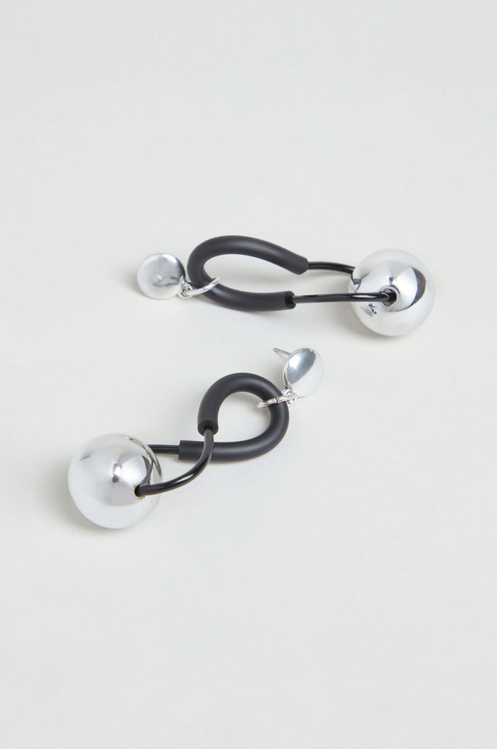 Infinity Earrings – A pair of modern drop earrings featuring large and small silver spheres connected by black curved elements, showcased against a light background. The sculptural design of the handmade Infinity Earrings reflects French artistry, blending unique elegance with contemporary style.