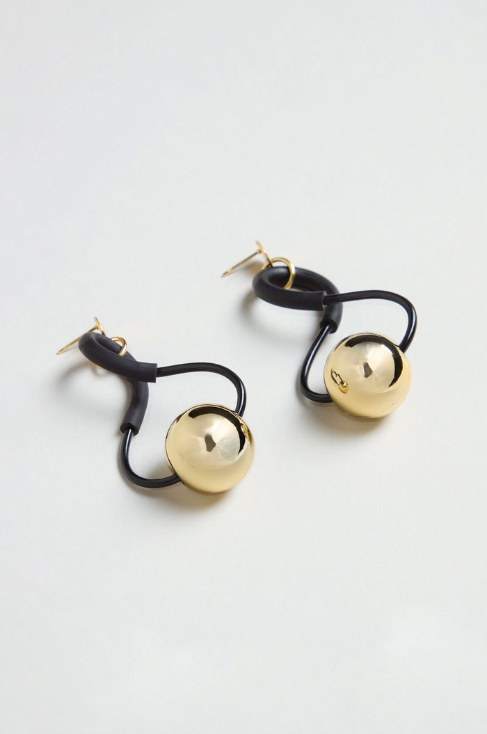 A pair of Infinity Earrings, featuring gold spherical pendants and sculptural black, irregularly looped attachments, displayed against a plain white background.