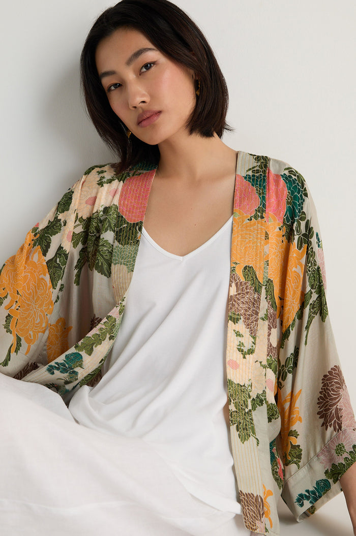 A woman with a straight bob wears a white top and the Jacquard Kimono, featuring a floral print and crafted from a soft modal cupro blend, as she poses against a plain light background.