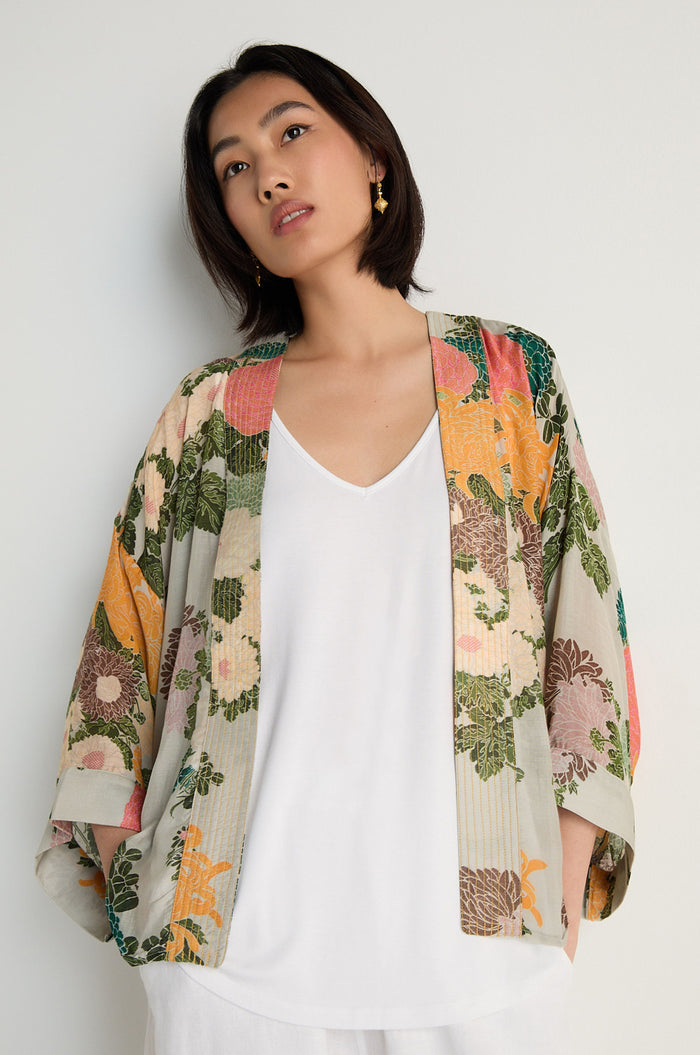 A person stands against a plain wall in a Jacquard Kimono, crafted from a luxurious modal cupro blend, layered over a white top. They look slightly upward with a neutral expression.