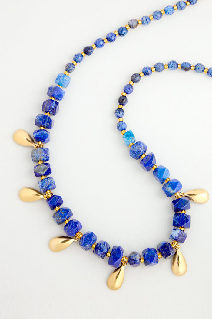 The Lapis Lazuli Teardrop Necklace features faceted blue stones and gold teardrop accents, handmade in Scotland and shown on a white background.
