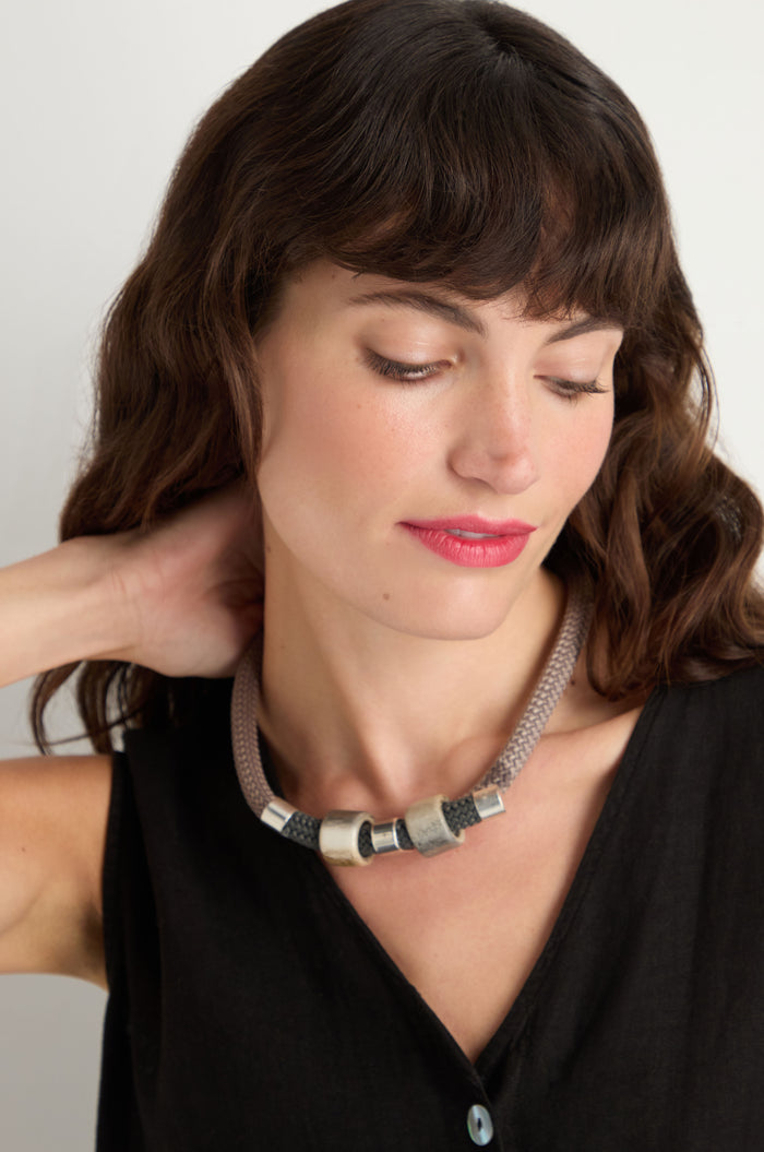 A woman with wavy brown hair wears a black sleeveless top and the Layered Marble Bead Cord Necklace, looking down with one hand behind her neck.