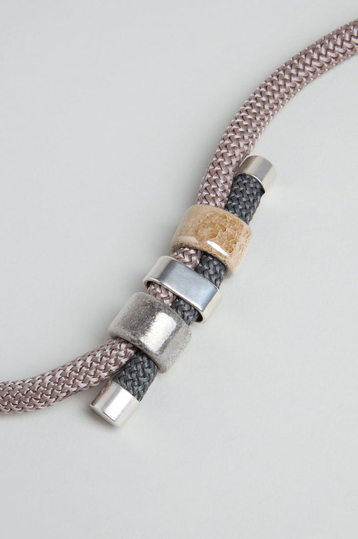 A detailed view of the Layered Marble Bead Cord Necklace showcases its braided cord and layered design, featuring metallic silver and beige marble-effect beads against a light background.