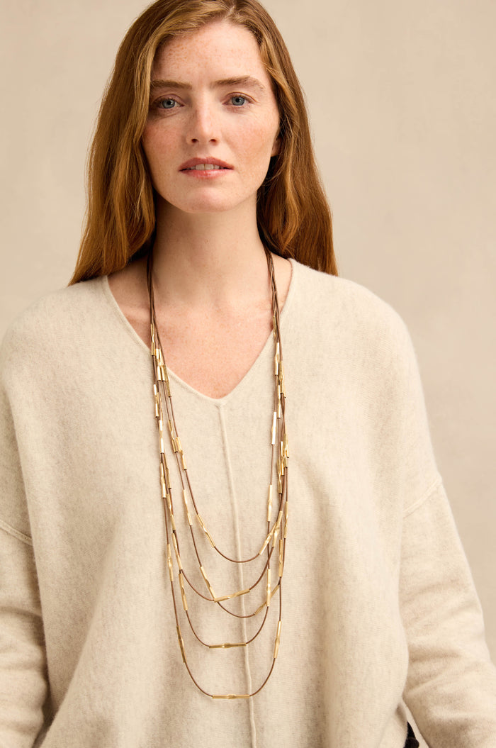A woman with long auburn hair wears a cream sweater and the Leather and Bead Cascade Necklace, standing against a plain beige background.