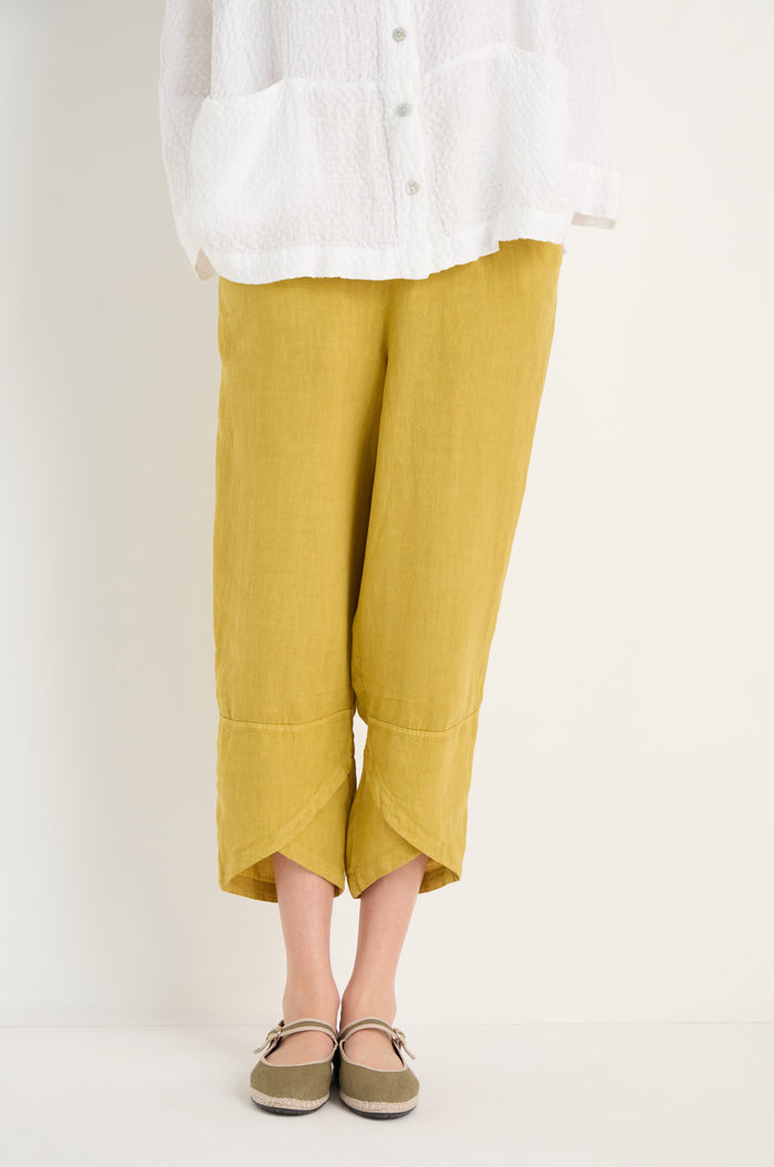 Person wearing a white textured shirt, Linen Tulip Hem Golden Bubble Trousers in mustard yellow, and brown Mary Jane shoes, standing against a plain light background.