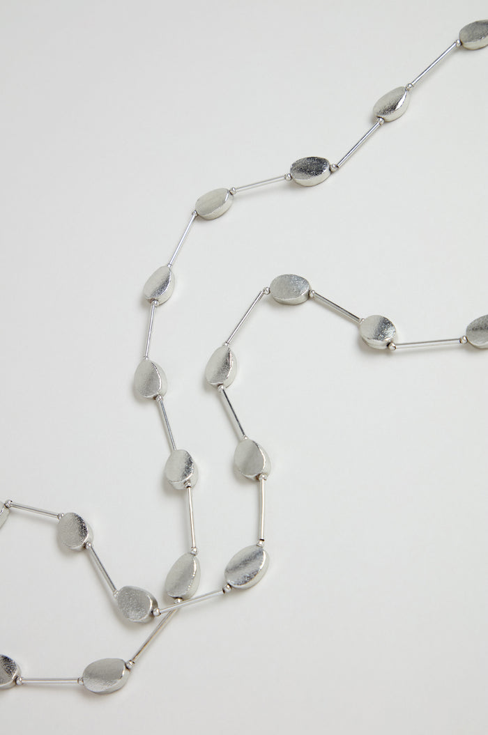 The Long Oval Disc Necklace showcases textured oval discs and slim connecting bars, elegantly displayed on a white background.