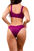 Back view of Merritt Dipped Cheeky Bikini Bottom in purple showcasing V-dipped cheeky back and no-show raw-cut fit on model with plain white background | alexhakim16 / M