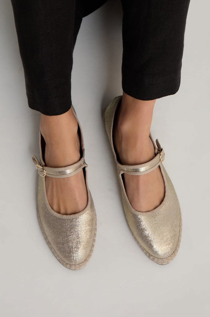 Wearing black pants and Metallic Mary Jane Shoes—handmade in Spain with buckle straps and recycled bicycle tyre soles—standing on a light-colored surface.