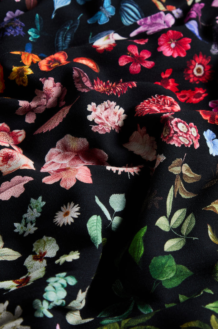Here’s a rewritten sentence using the product data: Close-up of black fabric adorned with a vibrant floral print in red, pink, green, and blue hues, as seen on the Midnight Garden Viscose Shirt.