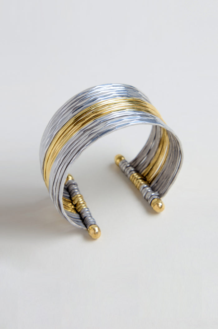 The Mixed Metal Cuff is a wide, open bracelet with layered silver and gold bands and gold-accented ends, shown against a light background.