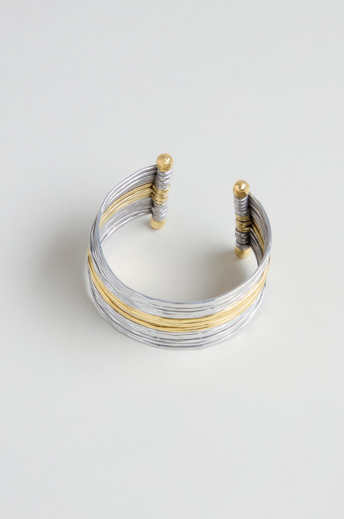 The Mixed Metal Cuff showcases silver and gold wrapped strands with gold-accented ends, creating a striking mixed metal bracelet displayed on a light background.