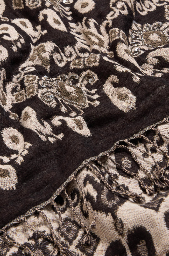 Close-up of the Motif Sequin Scarf, showcasing an abstract black and beige pattern in a neutral palette with decorative embroidery, subtle metallic sequins, and fringed edges. Crafted from a soft cotton-wool blend, this piece exudes effortless sophistication.