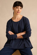 A woman with straight dark hair, wearing the Navy Cotton Jersey Pocket Top and jeans, sits with her arms crossed against a plain beige background.