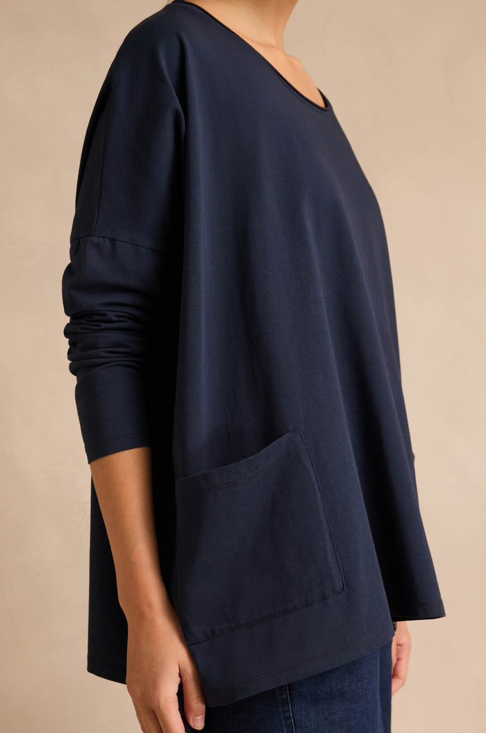 A person is wearing the Navy Cotton Jersey Pocket Top—an oversized casual style with long sleeves and a large front pocket—standing against a neutral background.