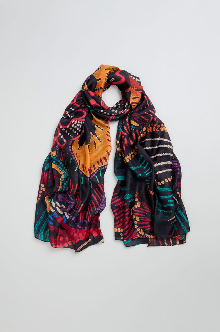 The Painted Firework Silk Scarf is a lightweight, colorful silk accessory with abstract orange, red, purple, green, and black patterns shown on a light background.