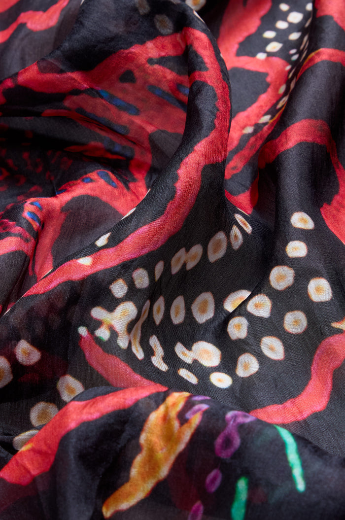 Close-up of the Painted Firework Silk Scarf, a lightweight accessory featuring a colorful abstract print with red, white, orange, and purple shapes on a black background.